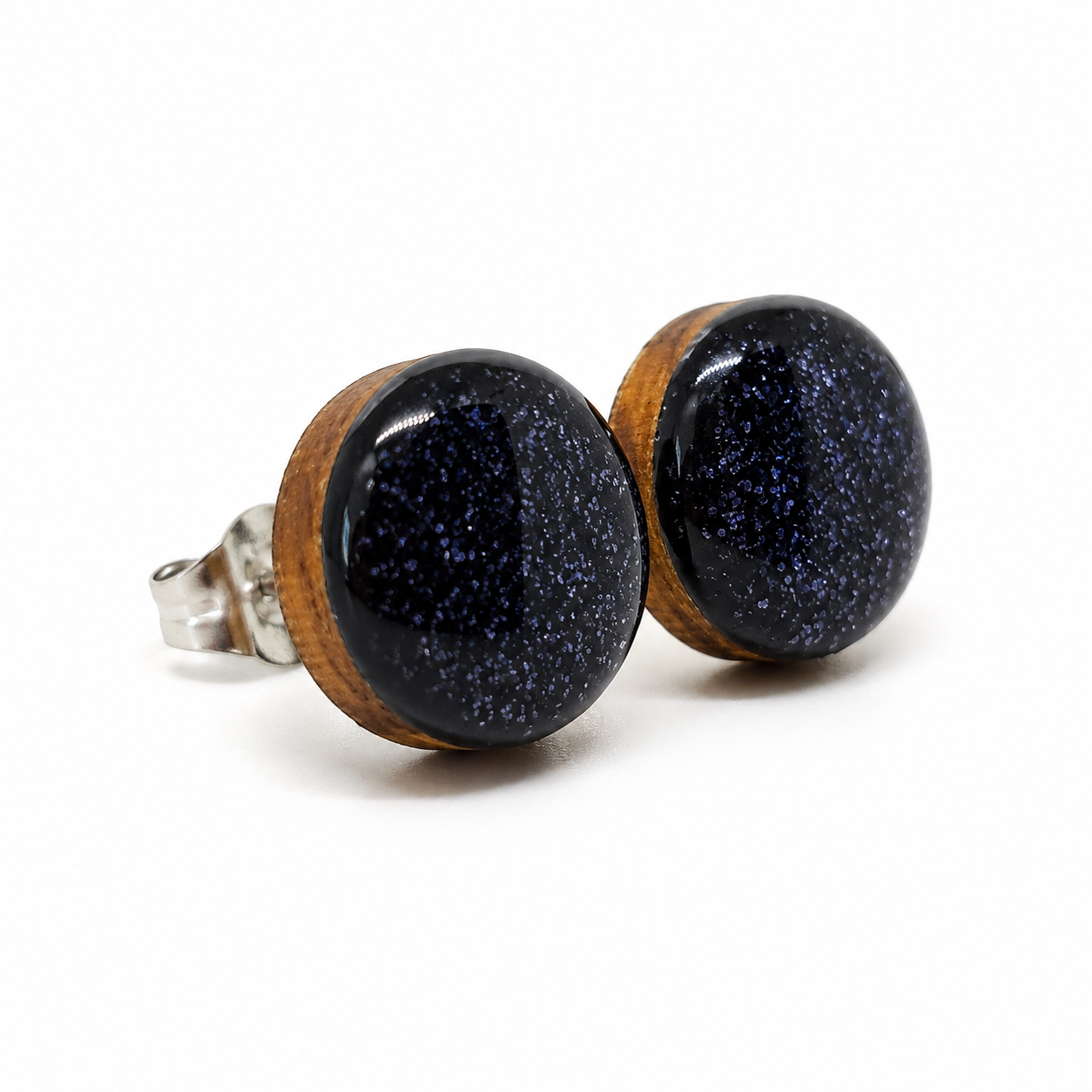 Pair of earrings with black speckled stones and wooden bases on a white background