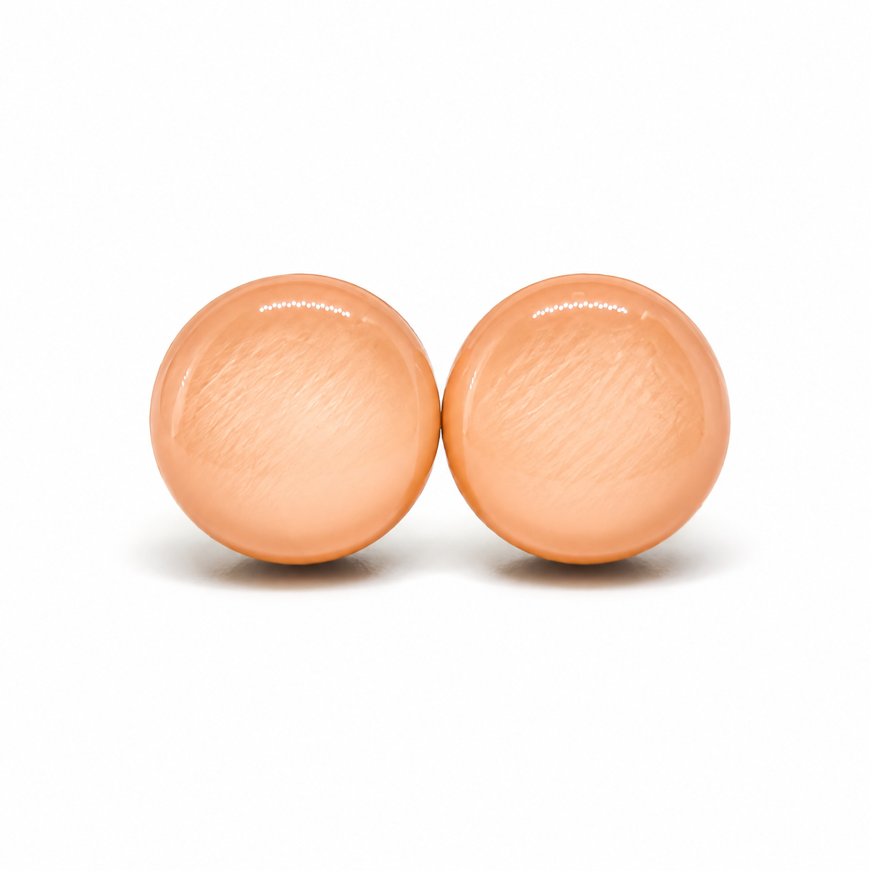 Two peach-colored stud earrings balls by candi cove designs on a white background